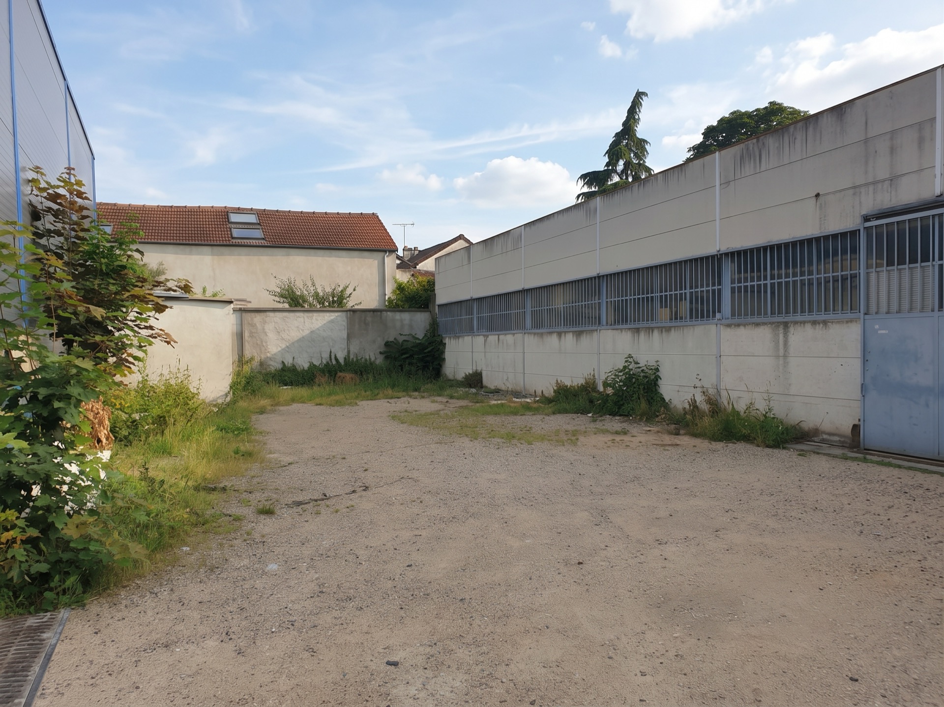 Façade du local au fond de la parcelle, long mur clair et porte métallique.